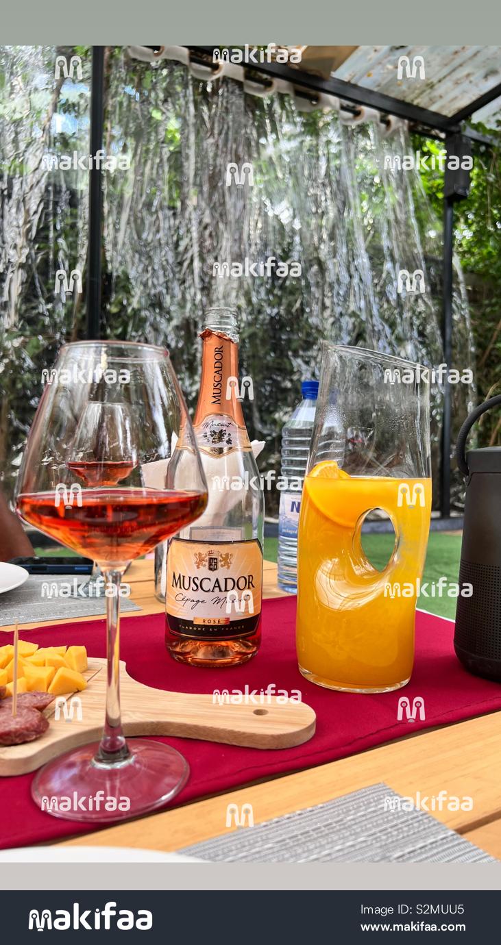 A glass of rosé wine with a bottle of Muscador and a modern pitcher of fresh orange juice
