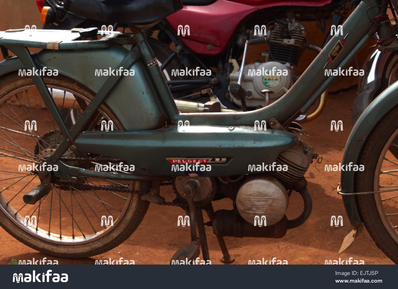 Moto Peugeot 103 vintage garée sur terre battue rouge, vue latérale détaillée