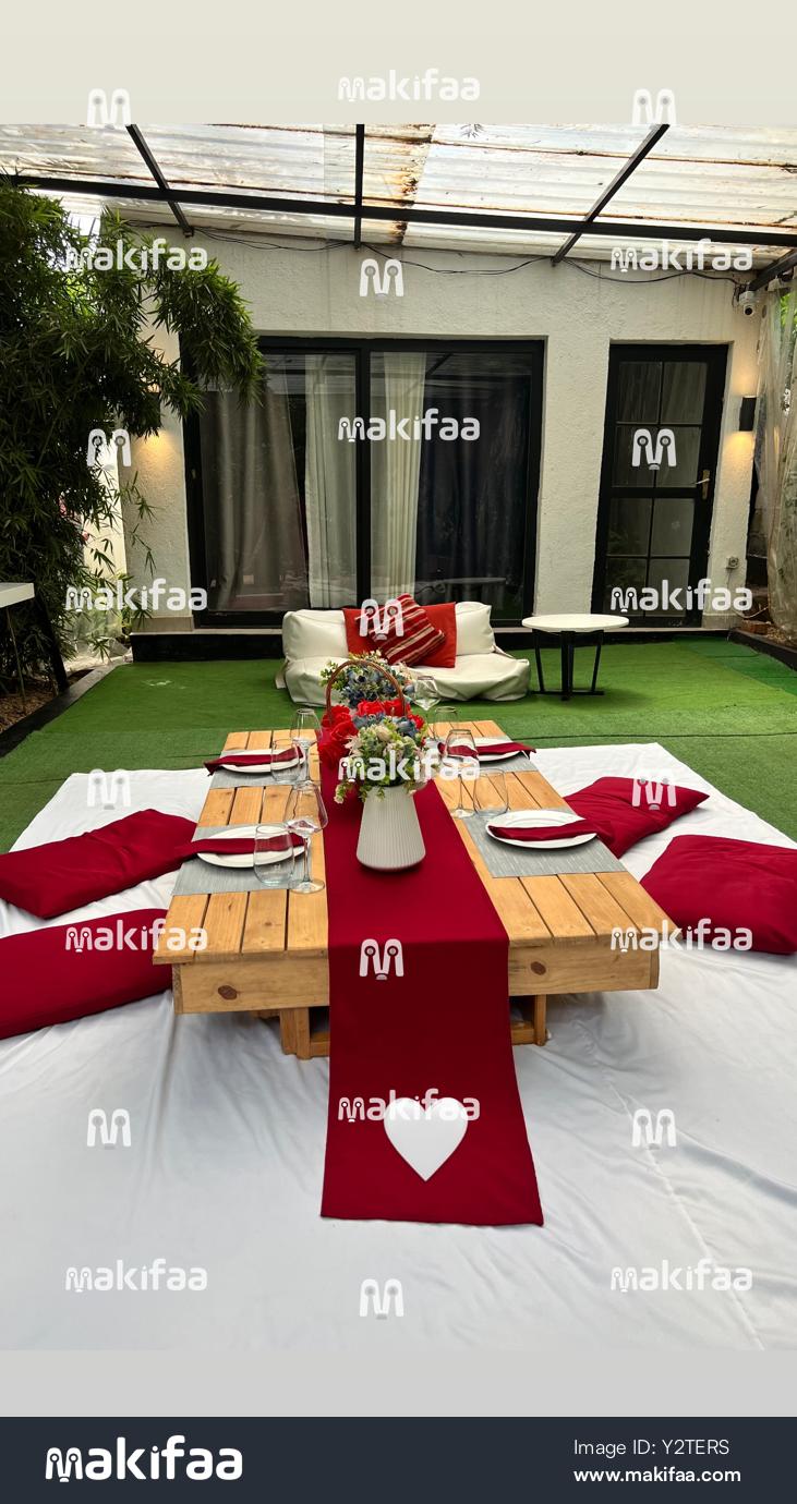 Table à manger romantique  accompagnée de coussins rouges sur gazon