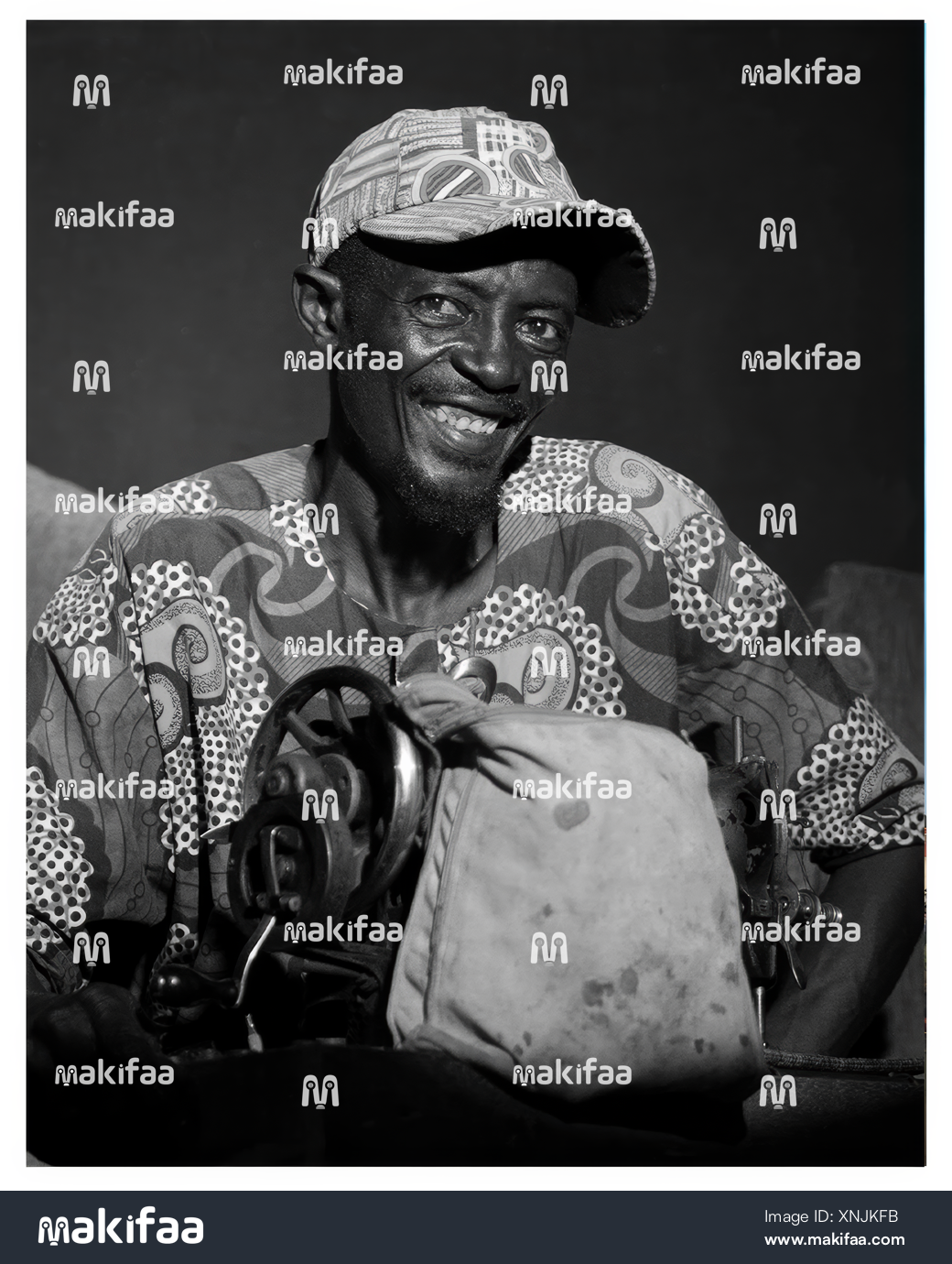 Black and white portrait of a smiling tailor in front of his sewing machine 