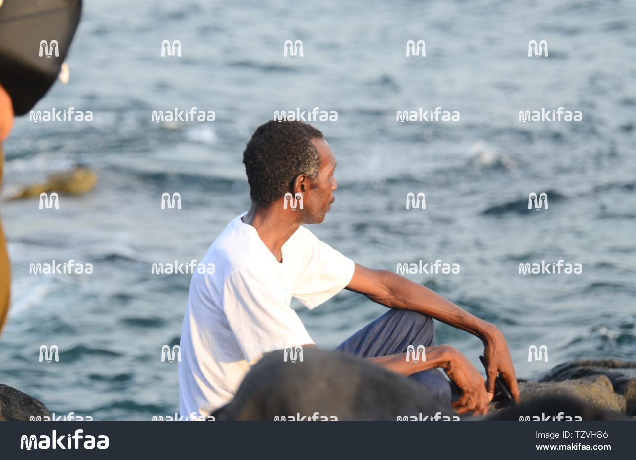 Um homem sentado sobre rochas à beira-mar.