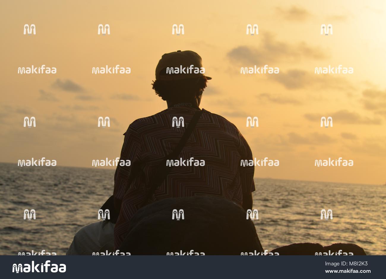 Un homme assis face à la mer au coucher du soleil