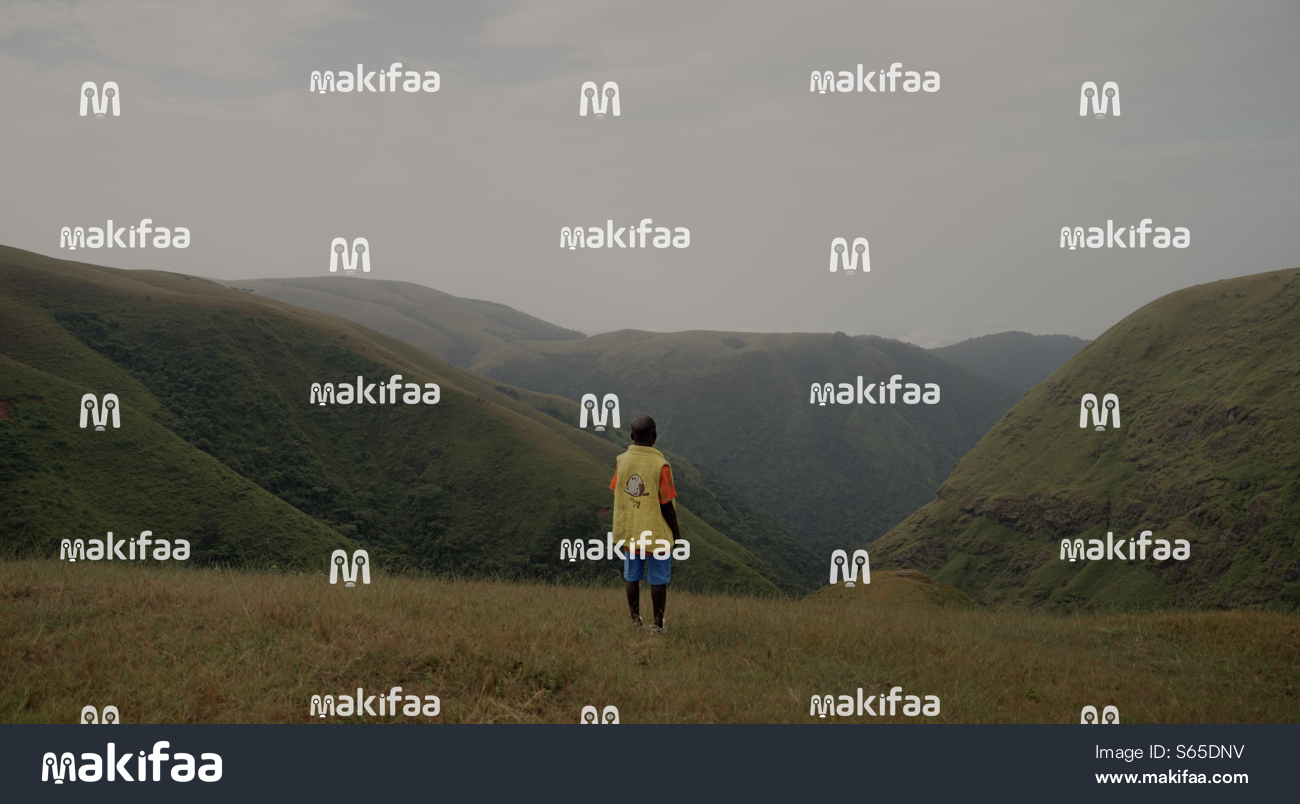 Un niño de pie en una colina mirando hacia un valle de montaña verde. 