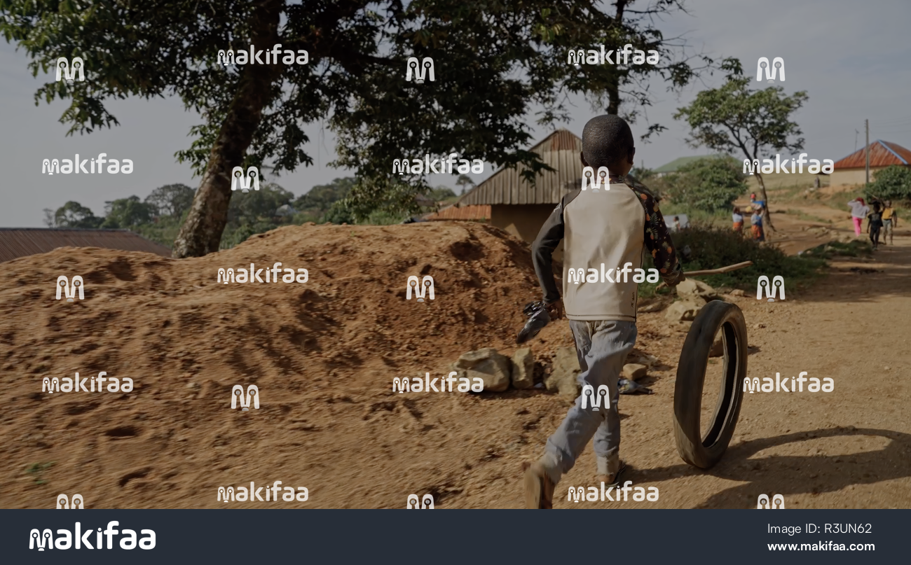 A child playing with a tire on a dirt road 