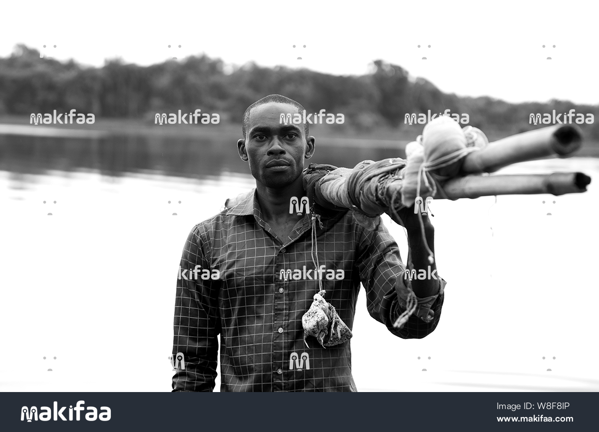 A man standing at the water&#39;s edge with a bundle of wood 