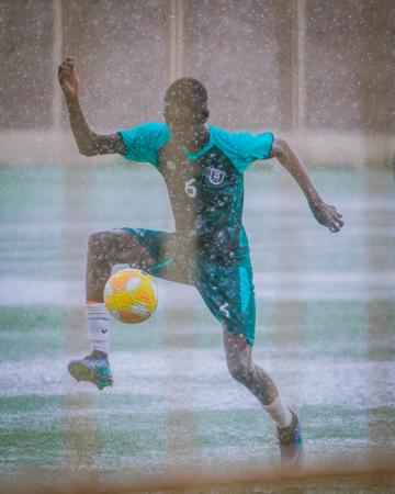 Joven jugando al fútbol bajo la lluvia 