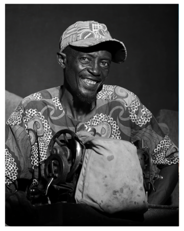 Black and white portrait of a smiling tailor in front of his sewing machine