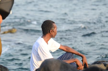 Um homem sentado sobre rochas à beira-mar.