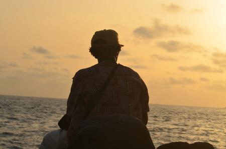 Un homme assis face à la mer au coucher du soleil
