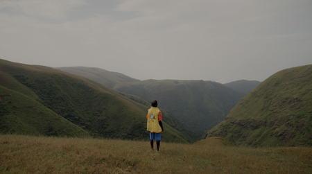 Un niño de pie en una colina mirando hacia un valle de montaña verde.