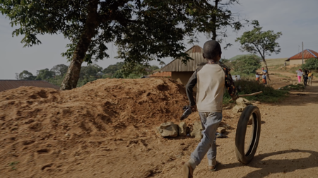 A child playing with a tire on a dirt road