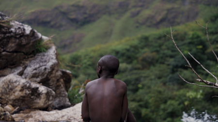 A boy sitting on a rock facing the green mountains