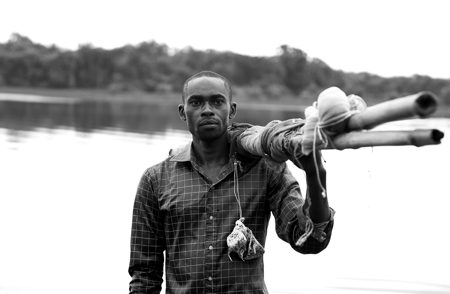 A man standing at the water's edge with a bundle of wood