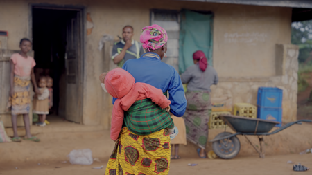 A woman carrying her child on her back in a rural setting